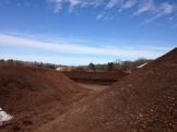 Large mounds of soil or mulch in an open outdoor area under a blue sky.