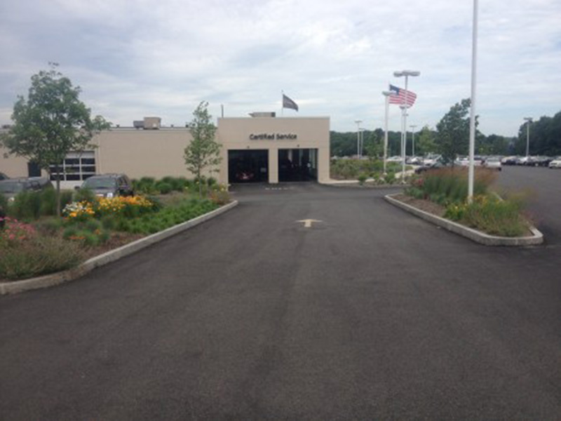 Entrance to a service building with landscaped flower beds and flags along the driveway.